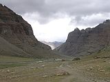 Tibet Kailash 08 Kora 10 View up Lha Chu Valley Entering the narrow valley on the western flank of Kailas, the place assigned to Amitabha, whose colour is red, he (the pilgrim) finds himself in a canyon of red rocks, the structure of which is so architectural in appearance that the pilgrim feels as if he is walking between rows of gigantic temples. They are adorned with elaborate rock-cornices, pillars, and ledges, and high above them there appears suddenly the dazzling ice-dome of Kailas. � Lama Anagarika Govinda: The Way of the White Clouds. You can just barely see Chuku Gompa on the hill to the left of the V in the valley.
